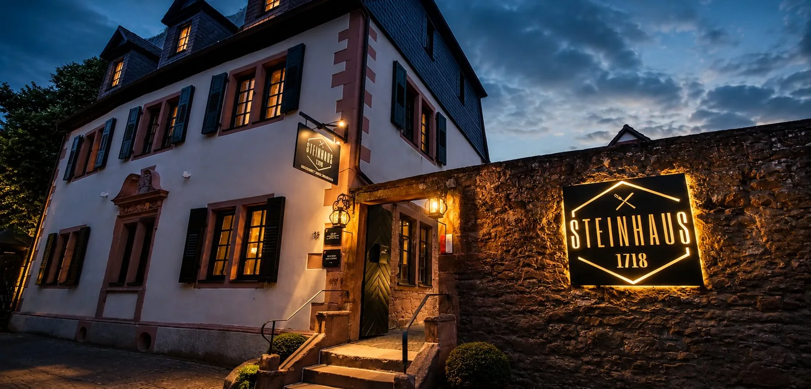 Steinhaus 1718 am Abend mit beleuchtetem Schild an der Stadtmauer
